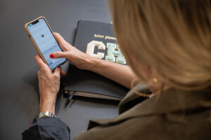 Person tippt auf einem Smartphone, daneben ein Notizbuch – Symbol für digitale Kommunikation und den Newsletter von Make It Matter.