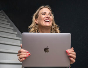 Kommunikationsberaterin von Make It Matter lacht und hält einen Laptop – Symbol für digitale Lernformate und praxisnahe LinkedIn-Trainings.